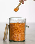 Hammered glass storage jar filled with red lentils with wooden lid and spoon.