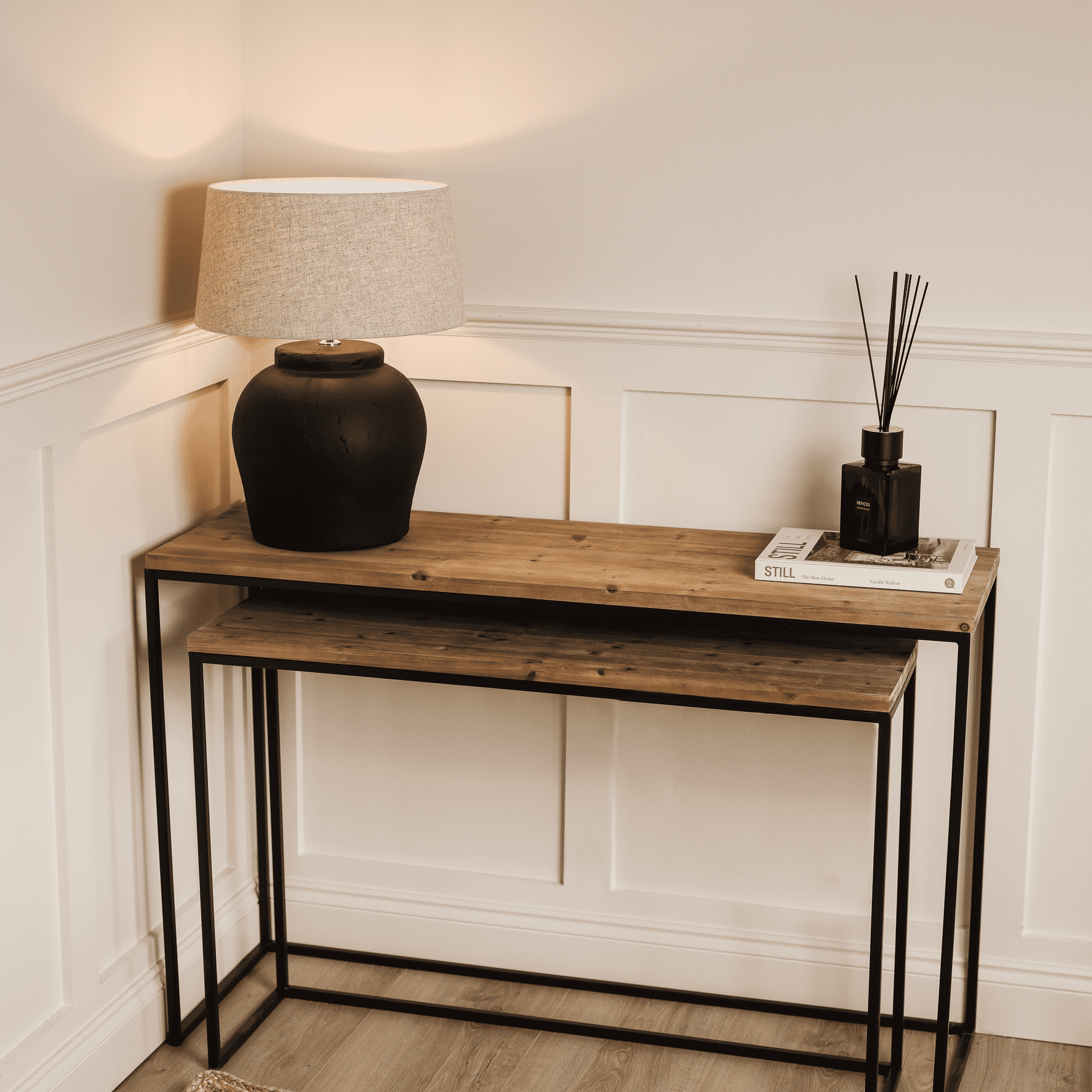 Two nest console tables with switched on black lamp, black diffuser and white coffee table book.