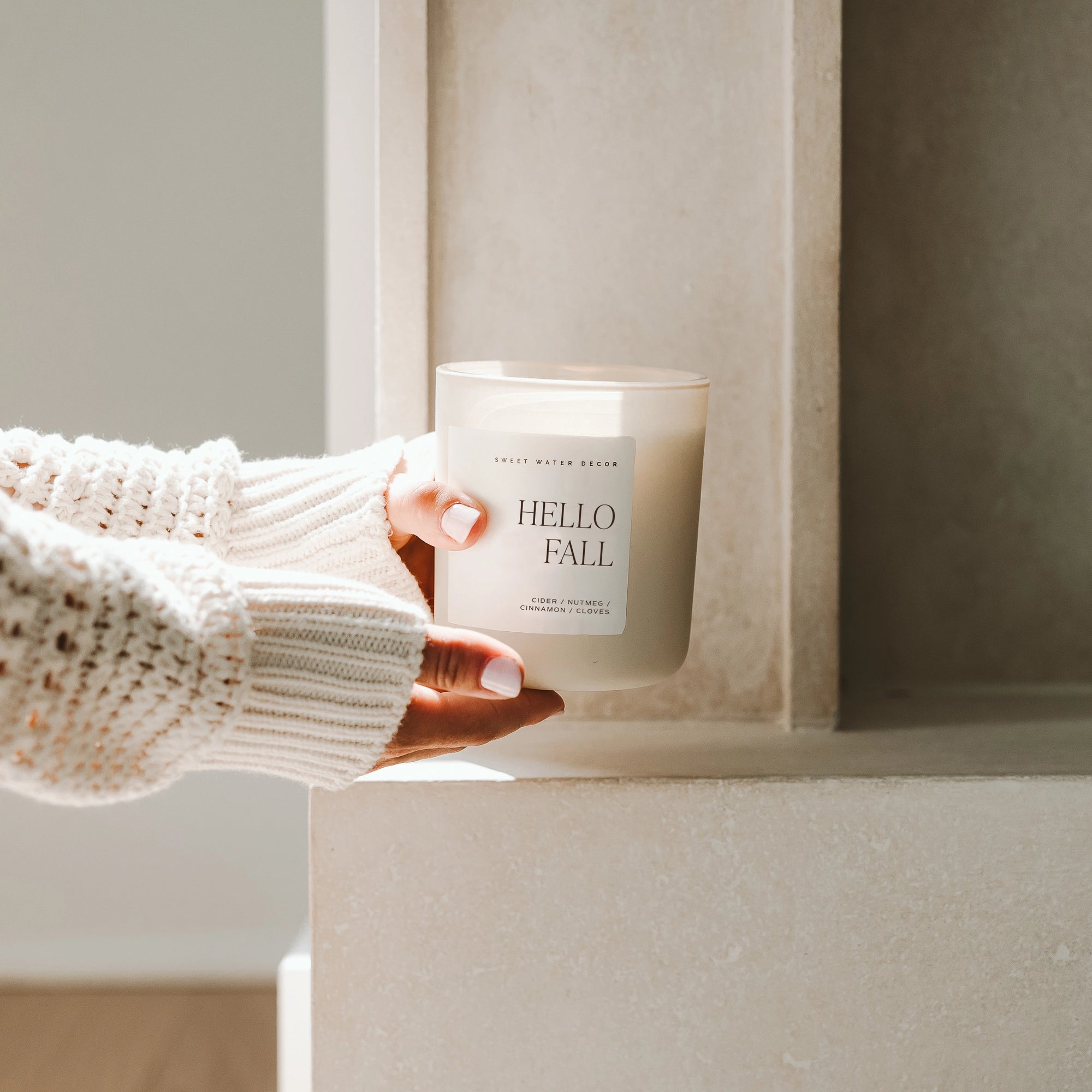 Soy candle in matte white jar, held up in two hands in natural sunlight.