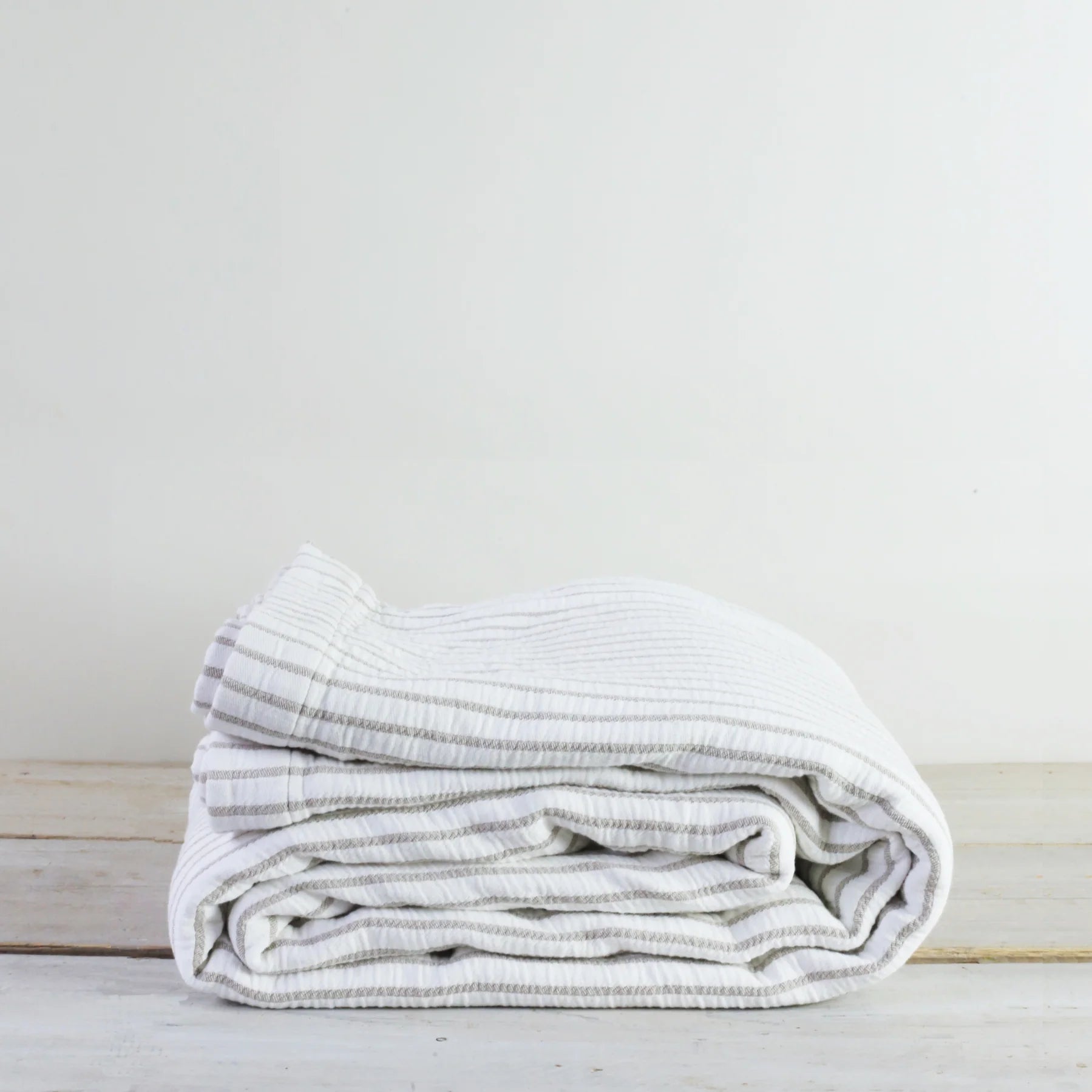 A folded Striped Cotton Throw Blanket on a rustic wooden floor.
