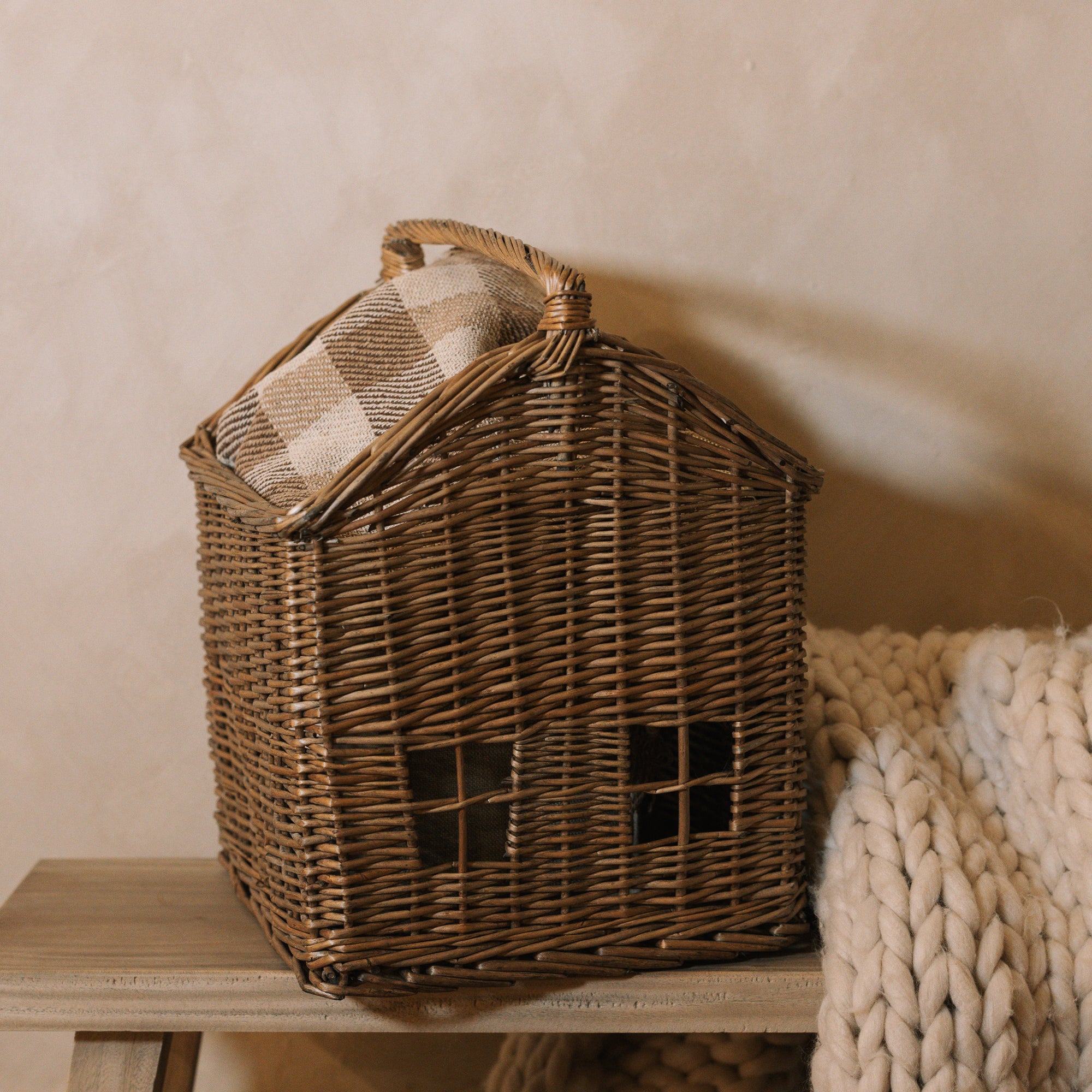 Woven basket with handle with chunky knitted throw on wooden bench.