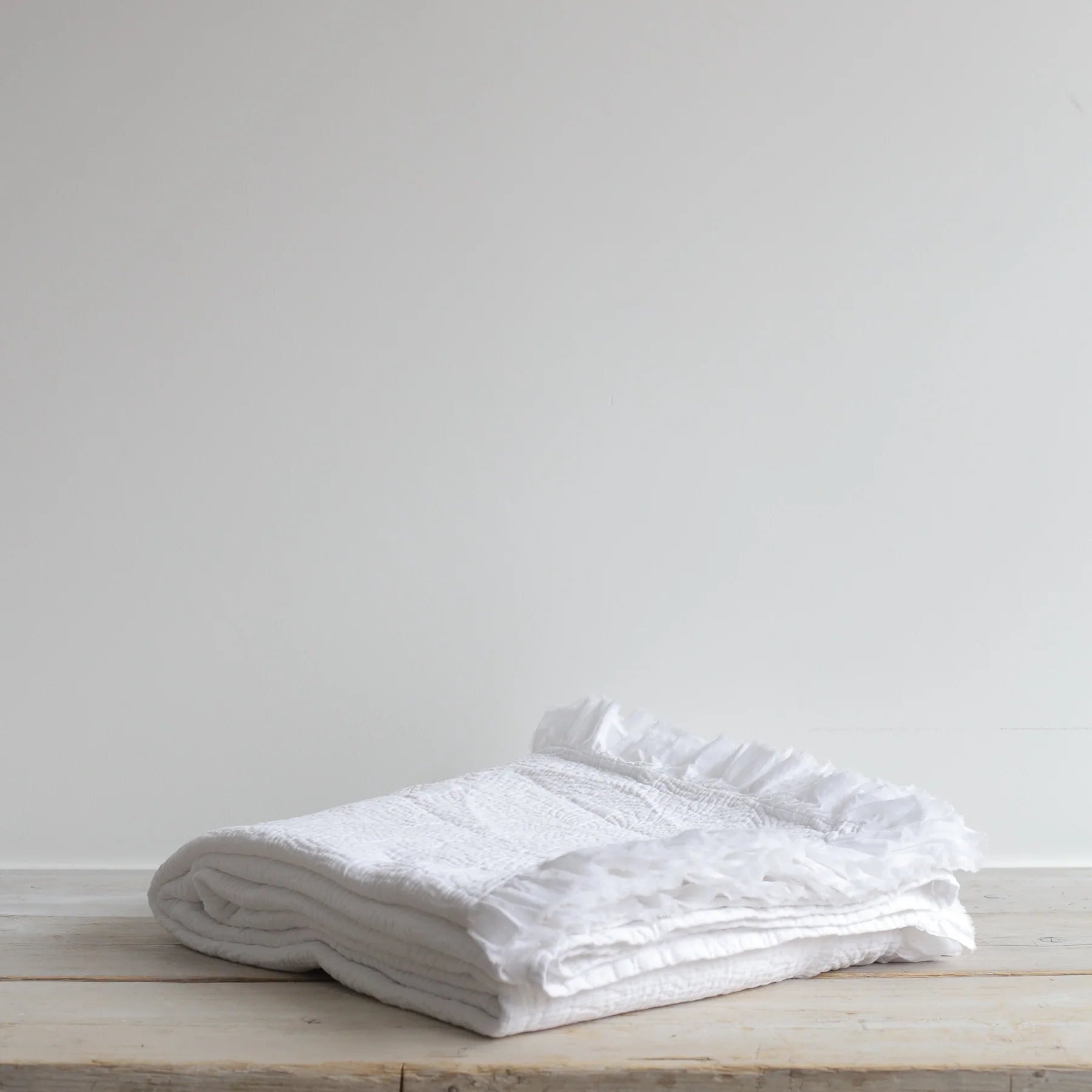 Textured White Bedspread folded neatly on a wooden table.