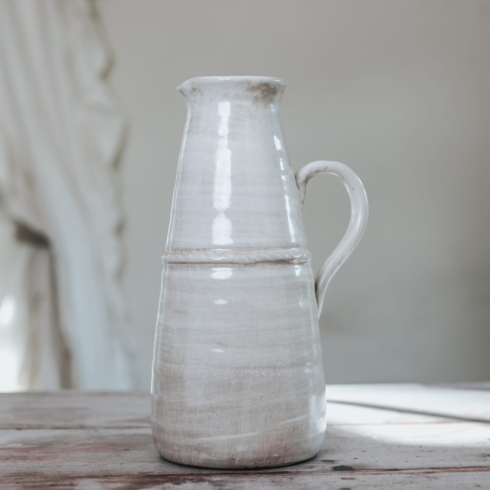 Creamy ceramic glazed vintage jug with handle on wooden table.