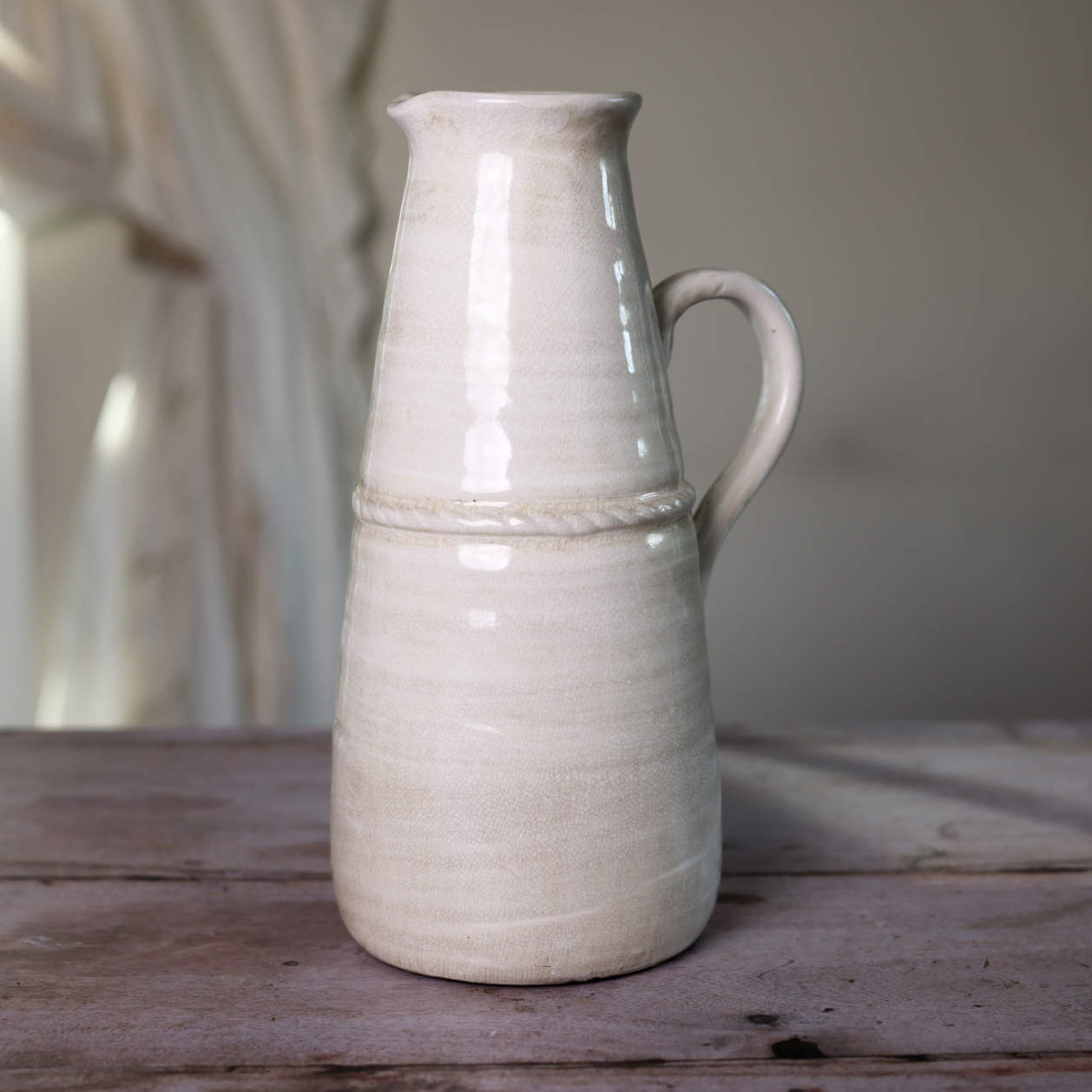 Cream vintage jug on wooden table with light reflection.