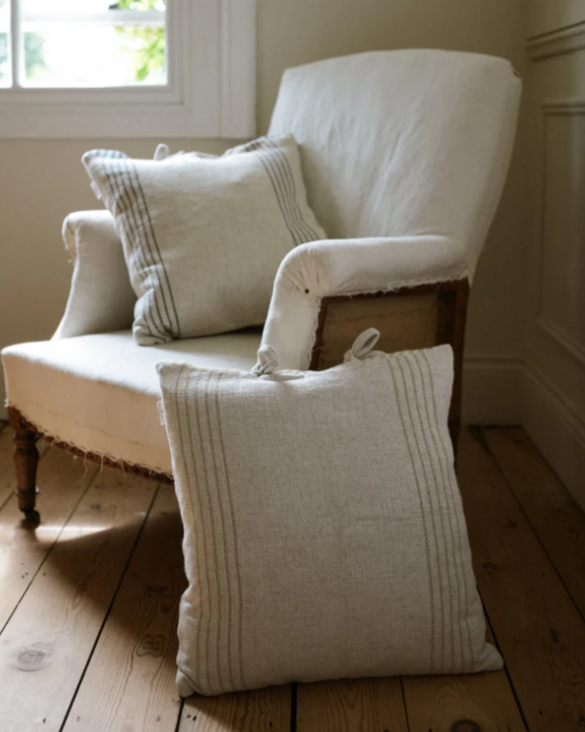 Striped cream cushion with bow ties leaning on an armchair.