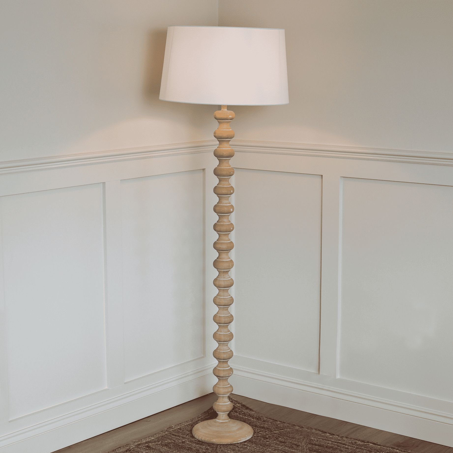 Wooden bobbin floor lamp lit with white linen shade in corner.