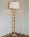 Wooden bobbin floor lamp lit with white linen shade in corner.