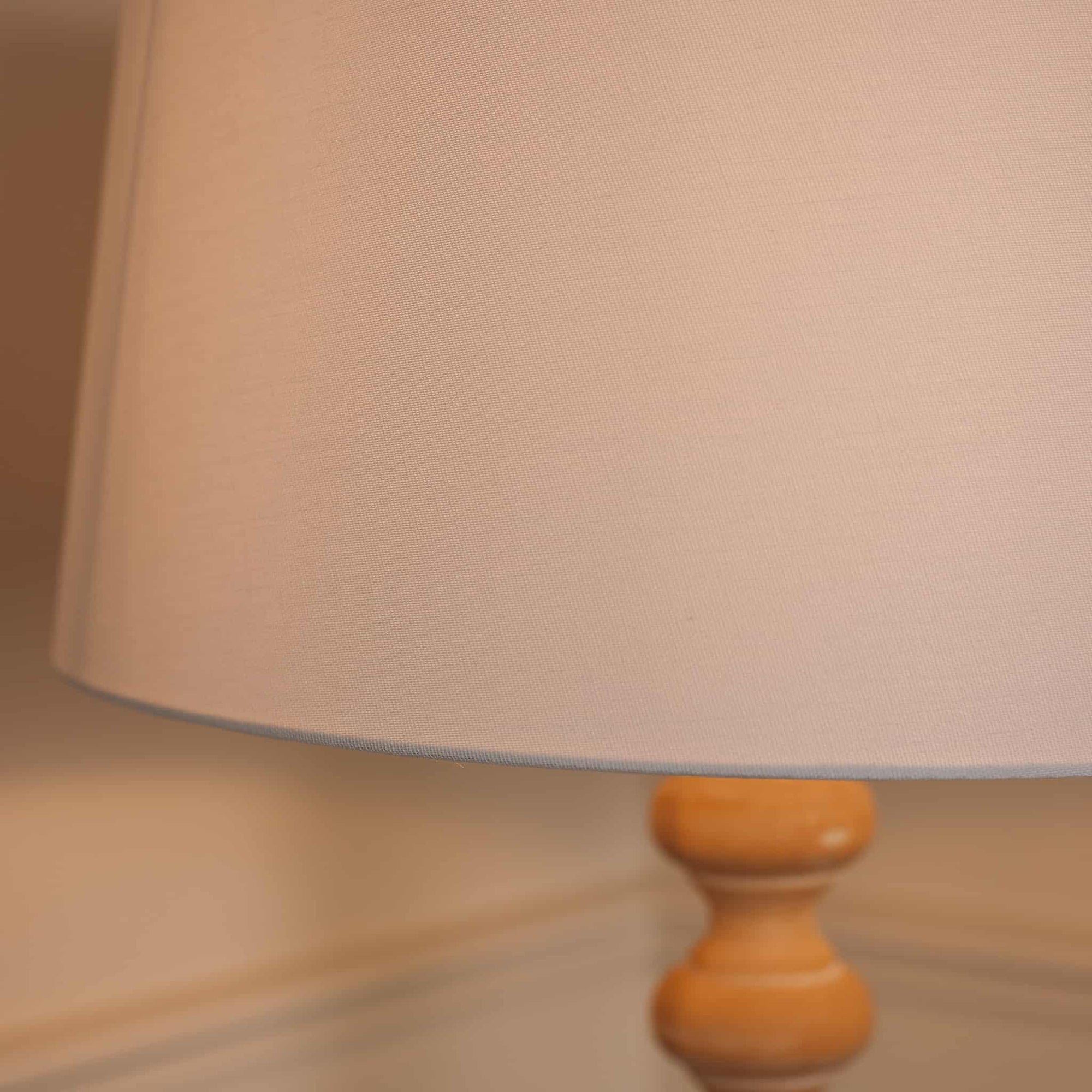 Close up of white linen lamp shade switched on wooden lamp.