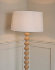 White linen lamp shade on wooden bobbin floor lamp.