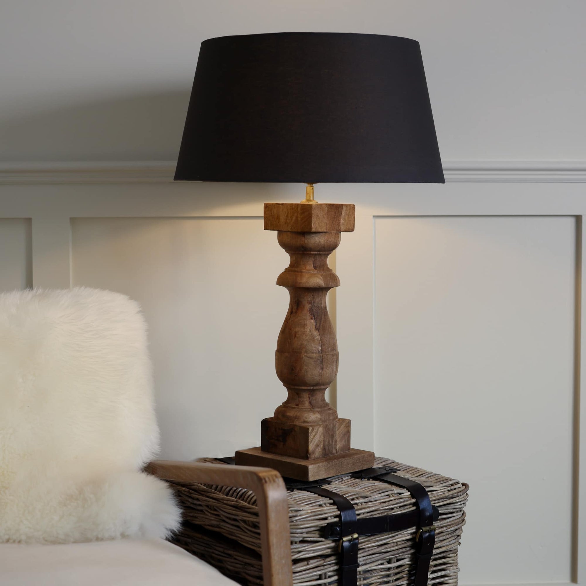 Tall column wooden lamp on side table with black shade, lit.