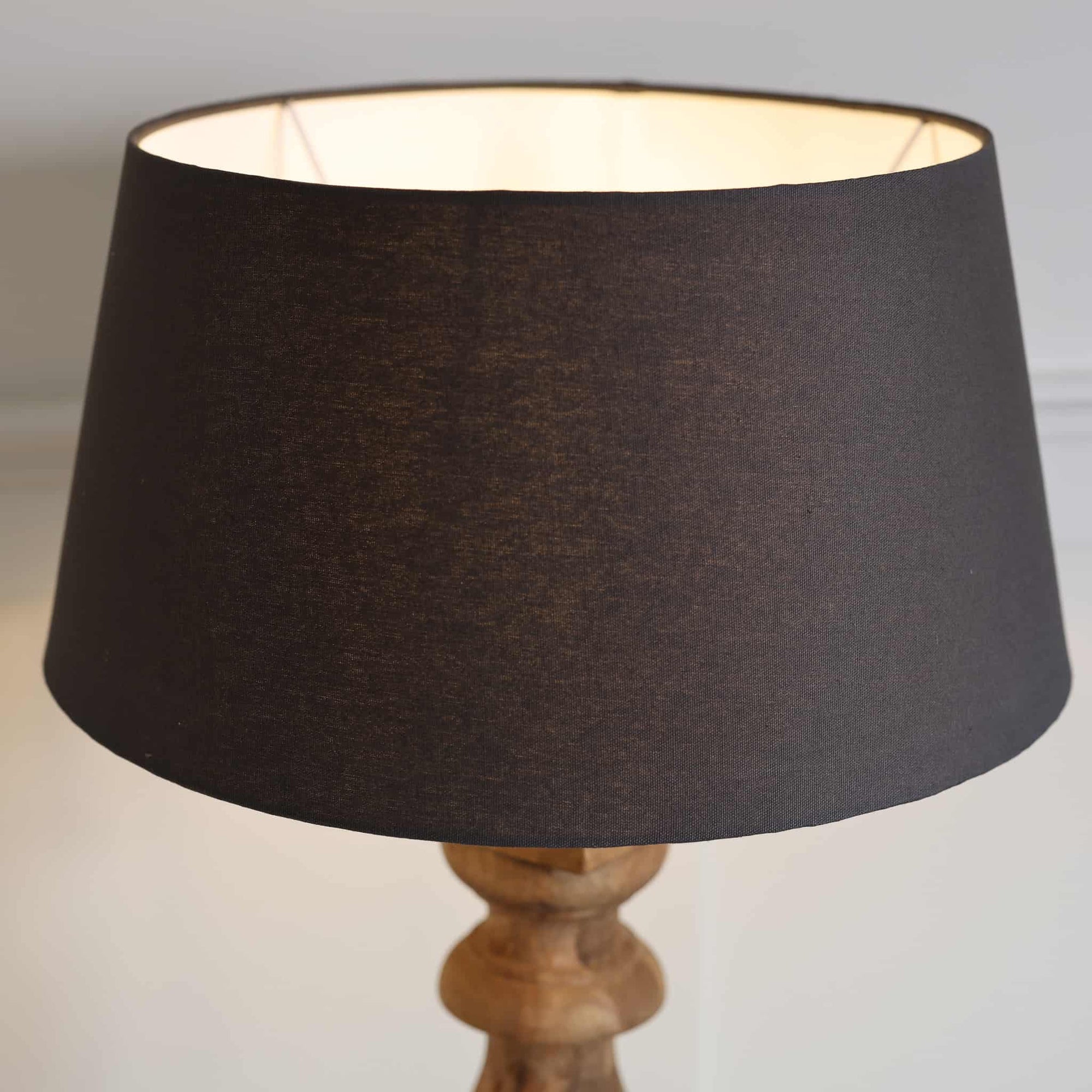Black cotton lamp shade on wooden base, with lamp switched on.