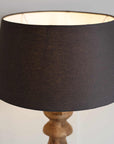 Black cotton lamp shade on wooden base, with lamp switched on.