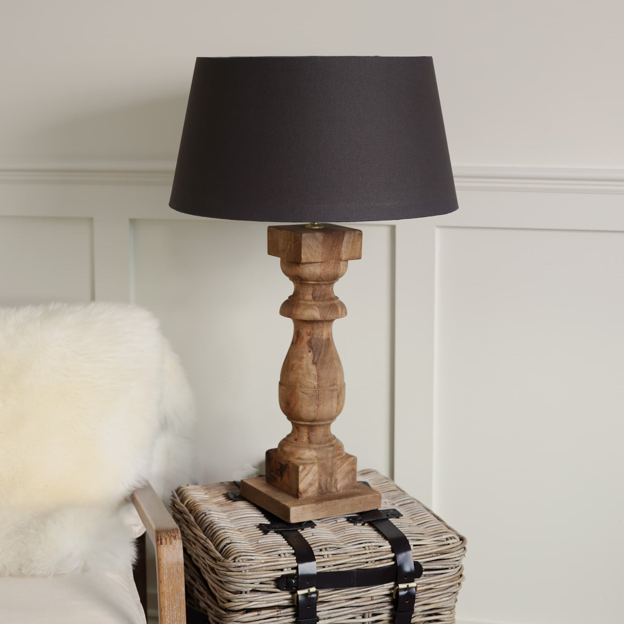 Tall column wooden lamp on side table with black shade.