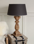 Tall column wooden lamp on side table with black shade.