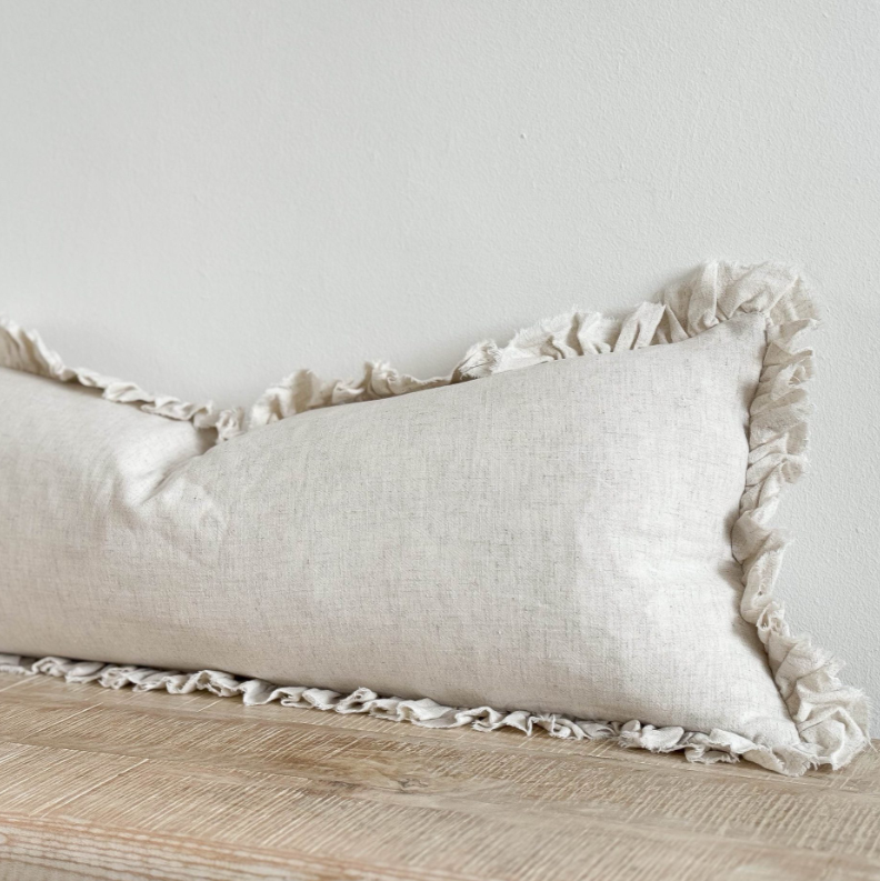 Close up of sand coloured bolster cushion with ruffled edge on wooden surface.