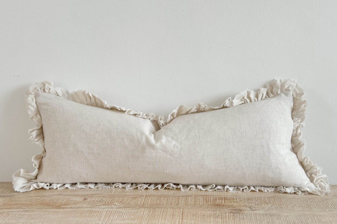 Sand coloured bolster cushion with ruffled edge on wooden surface.