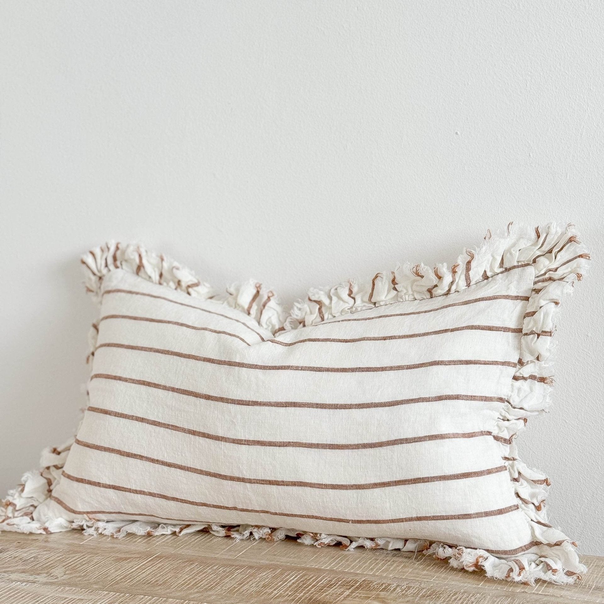 Brown and cream ruffle rectangle linen cushion on wooden surface.