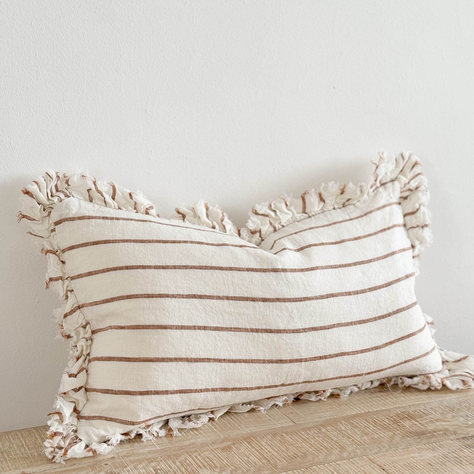 Brown and cream ruffle rectangle linen cushion on wooden surface.