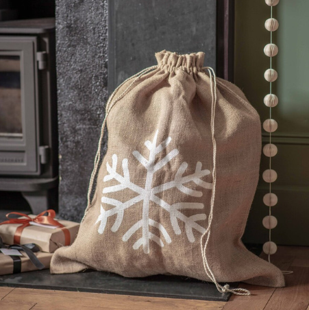 Jute Christmas sack with snowflake on, in front of the fireplace and filled with gifts.