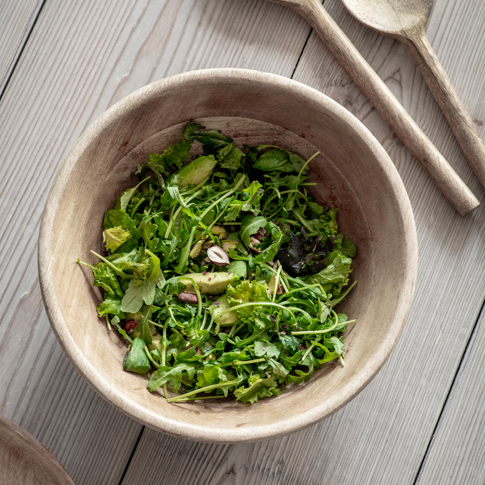 Wooden serving bowl with green salad on wooden table.