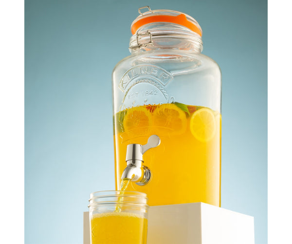 Kilner 5 litre round glass drink dispenser filled with orange pouring into glass.