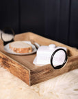 Wooden tray with black iron handles on a furry rug with butter and bread.