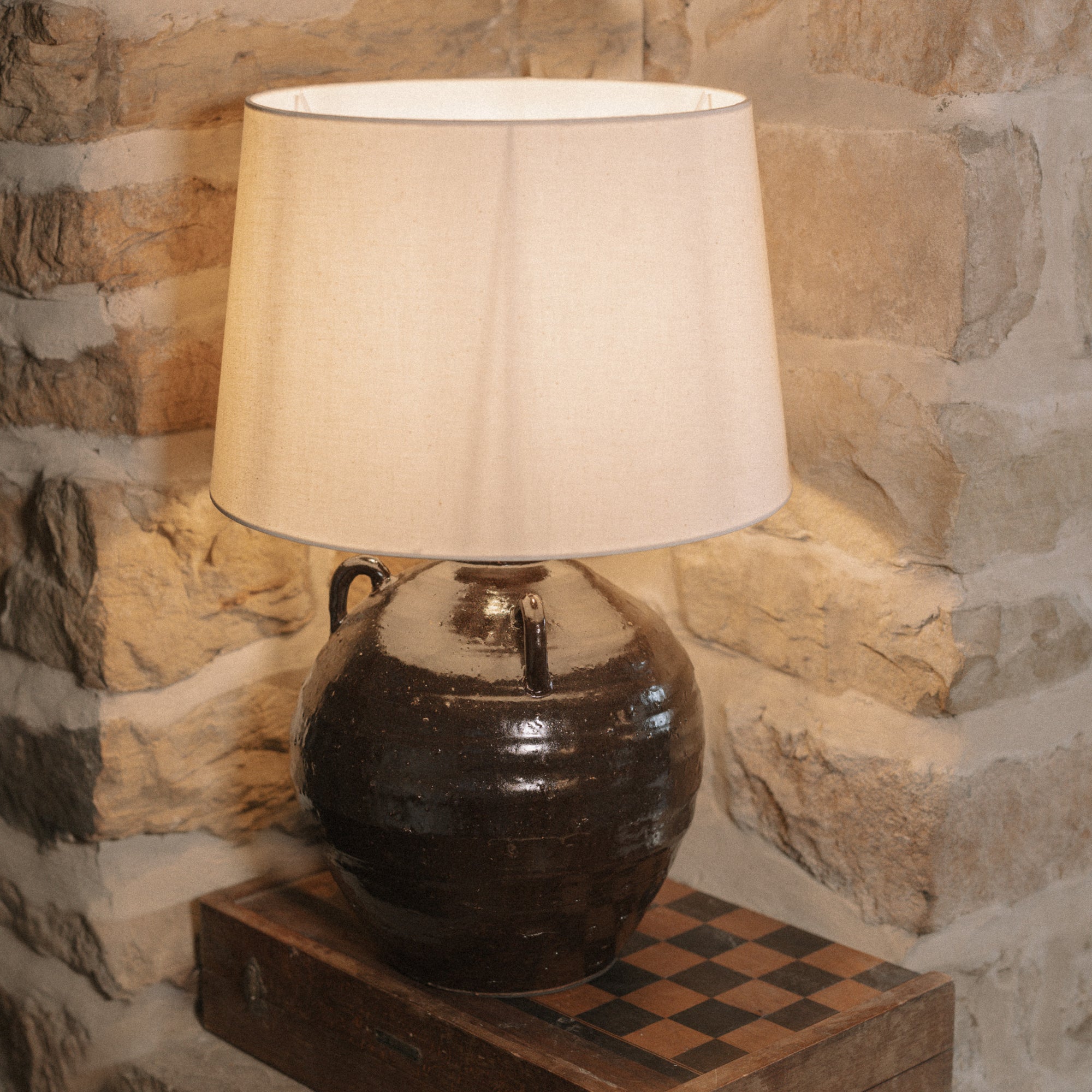 Large brown Table Lamp With Linen Shade on wooden chess board against stone wall. 