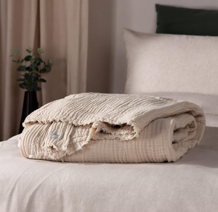 Natural cream crinkle cotton throw folded up on a bed.