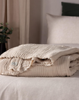 Natural cream crinkle cotton throw folded up on a bed.