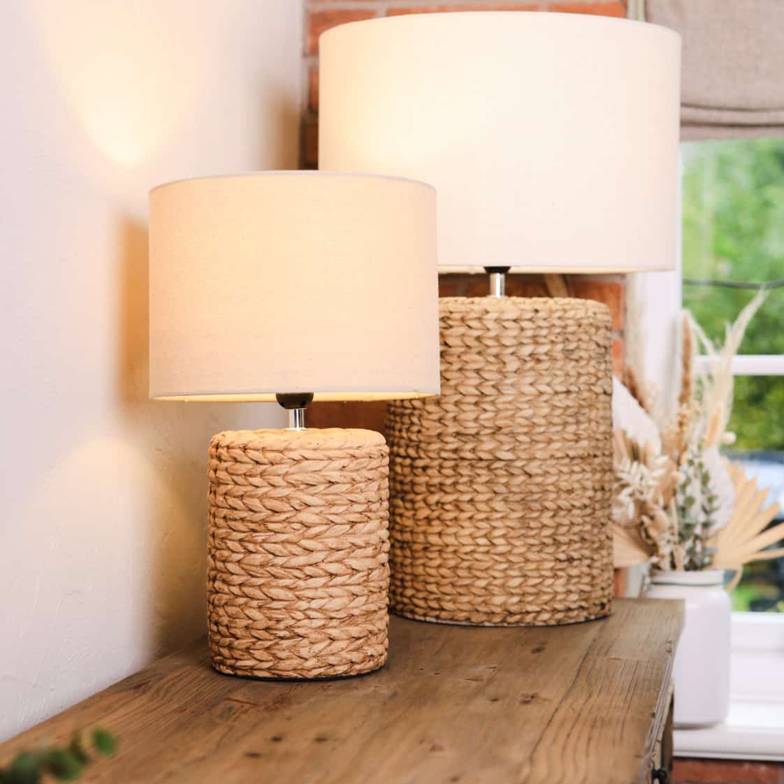 Pair of lamps with neutral rope effect base and light linen shade. Both switched on, on wooden console table.