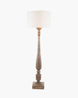 Tall brown column floor lamp switched on with square base and turns, with white lamp shade.