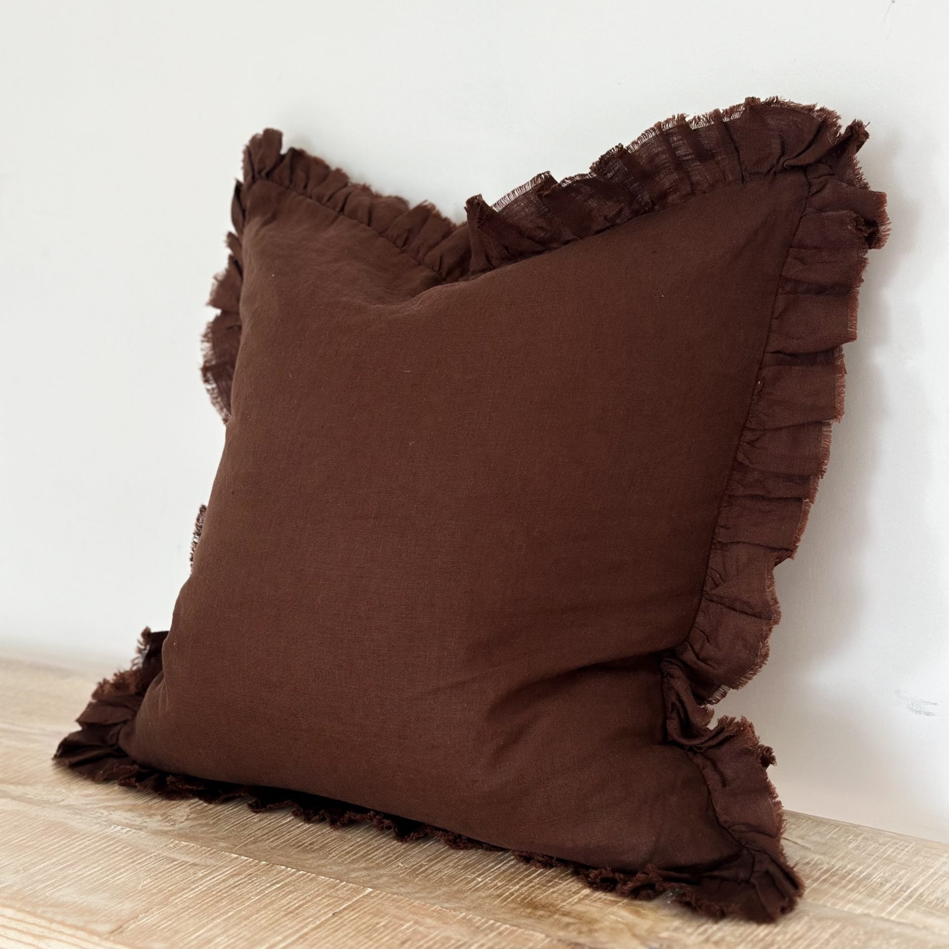 Large chocolate ruffle linen cushion on wooden surface.