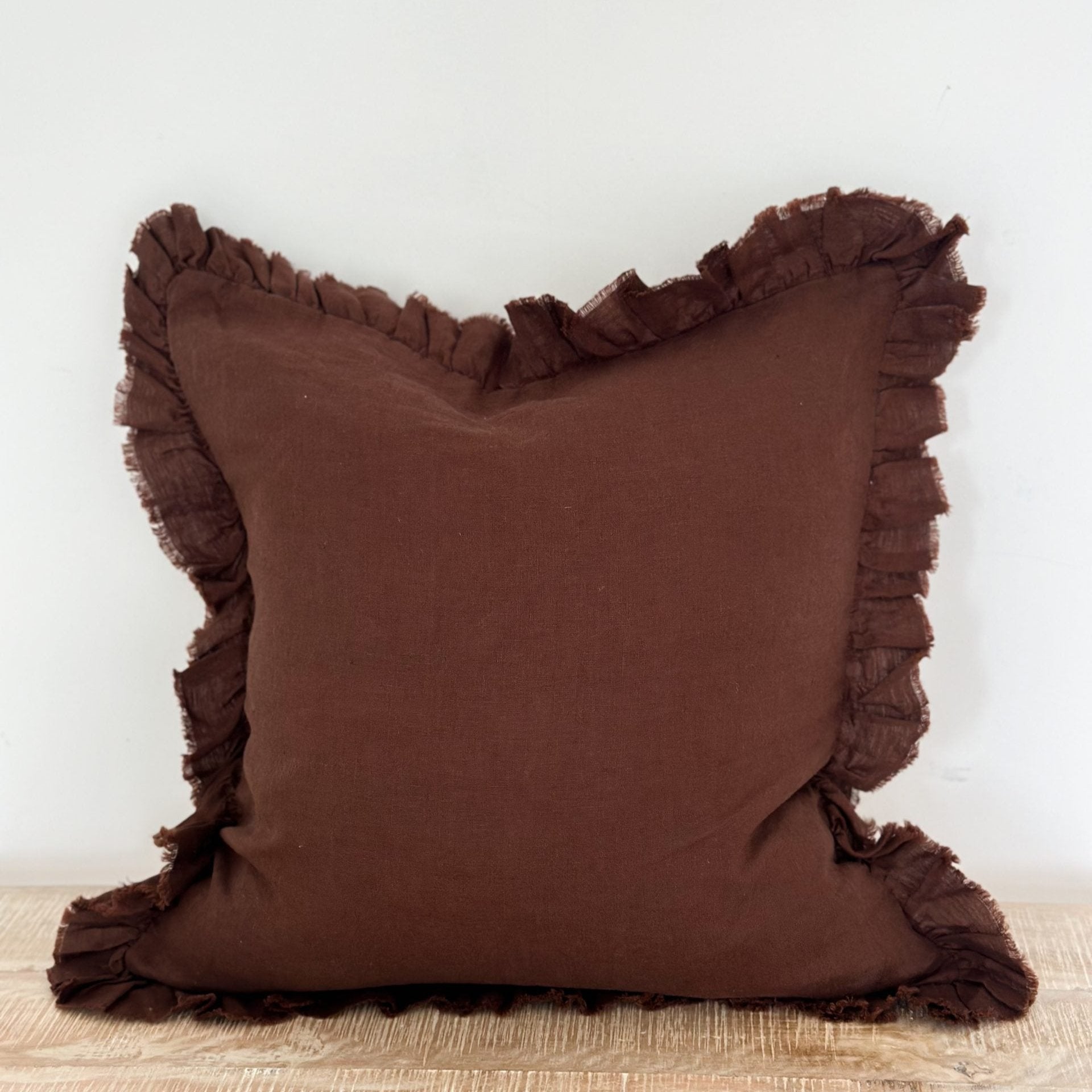 Large chocolate ruffle linen cushion on wooden surface.