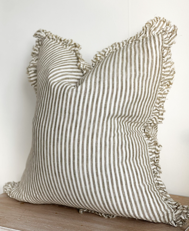 Olive and natural striped cushion with ruffled edge on a wooden surface.