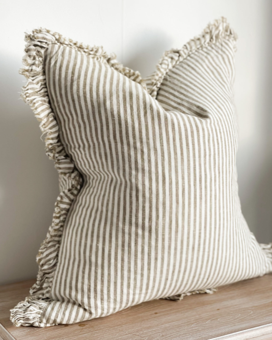 Olive and natural striped cushion with ruffled edge on a wooden surface.