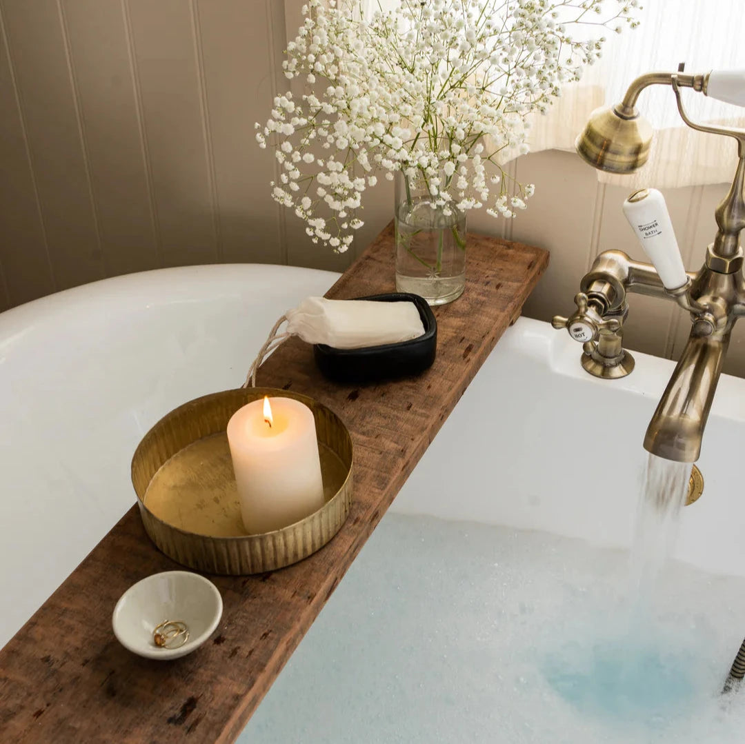 Brass metal reeded tray on bath plank, with pillar candle lit inside and other trinkets.