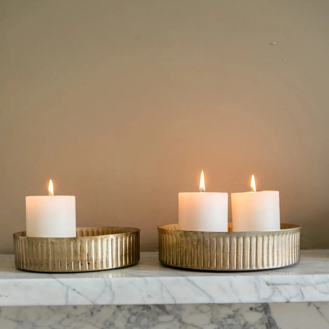 Set of two brass metal reeded tray with lit pillar candles, on marble shelf.