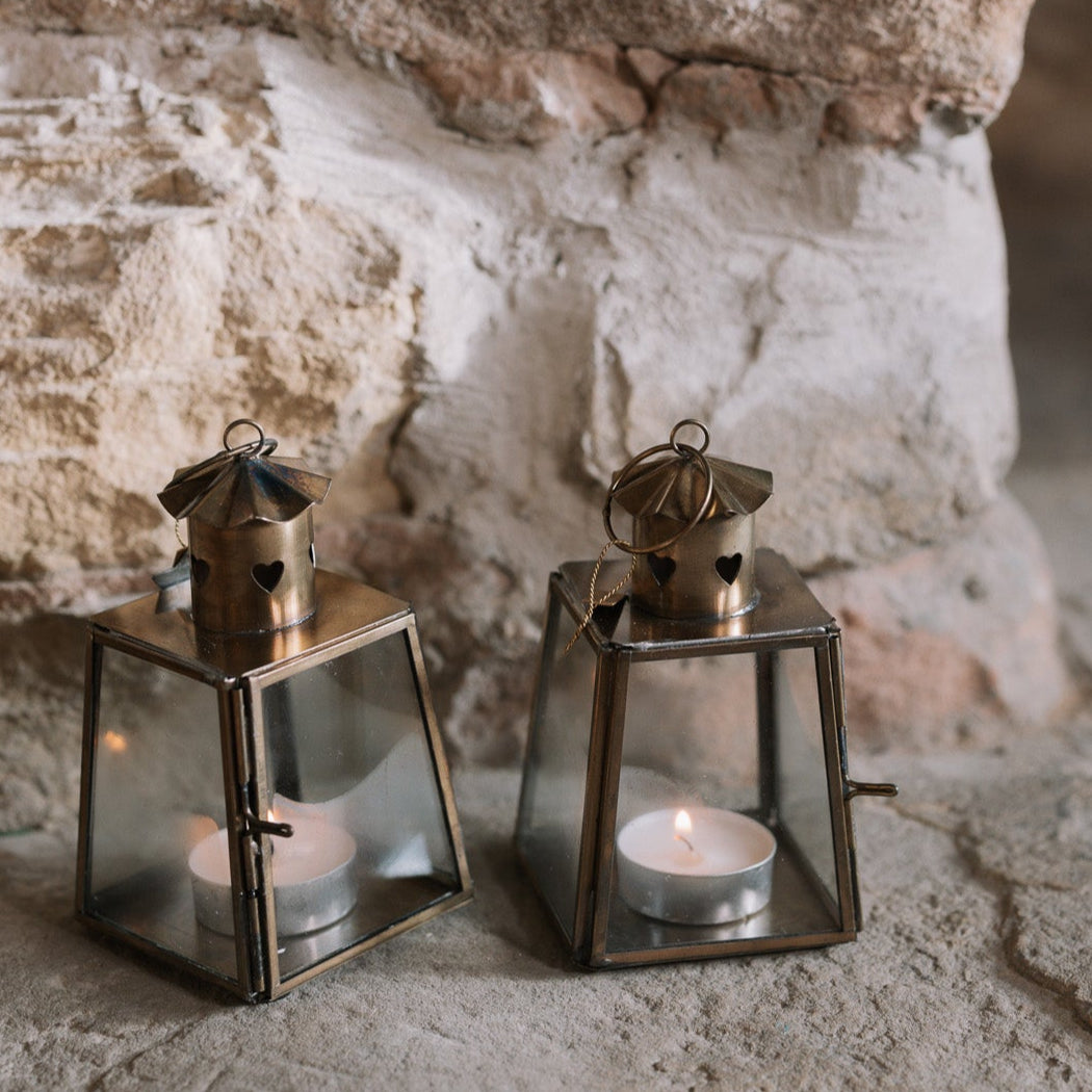 Two Mini bronze tealight candle lantern on stone hearth, with lit candles inside.