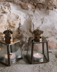 Two Mini bronze tealight candle lantern on stone hearth, with lit candles inside.