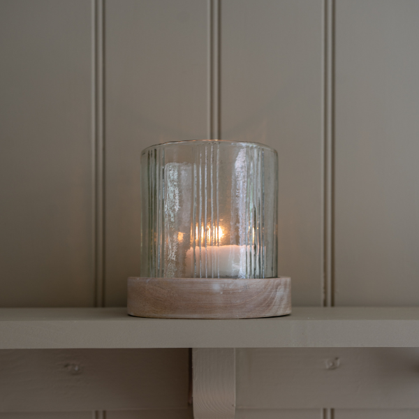 A rustic glass candle holder against a panelled wall.