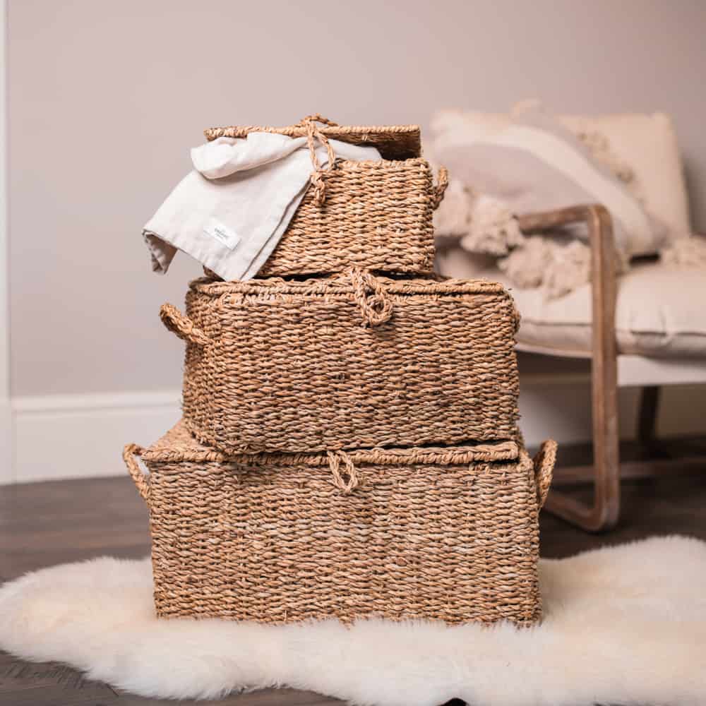 3 woven seagrass storage trunks piled up on furry rug.
