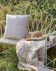 White outdoor bench with cushion and throws in garden.