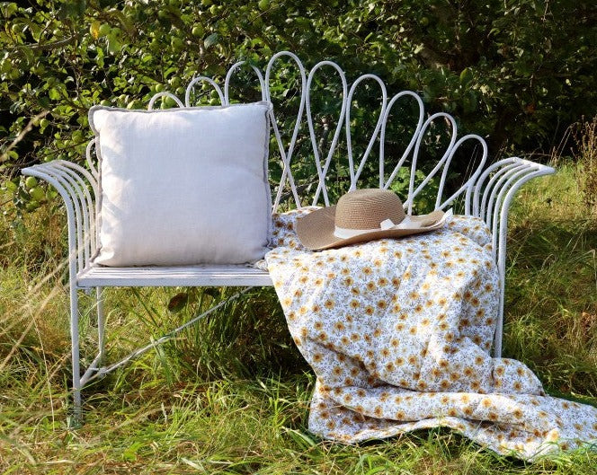 White outdoor bench with cushion and throws in garden.