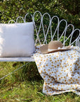 White outdoor bench with cushion and throws in garden.