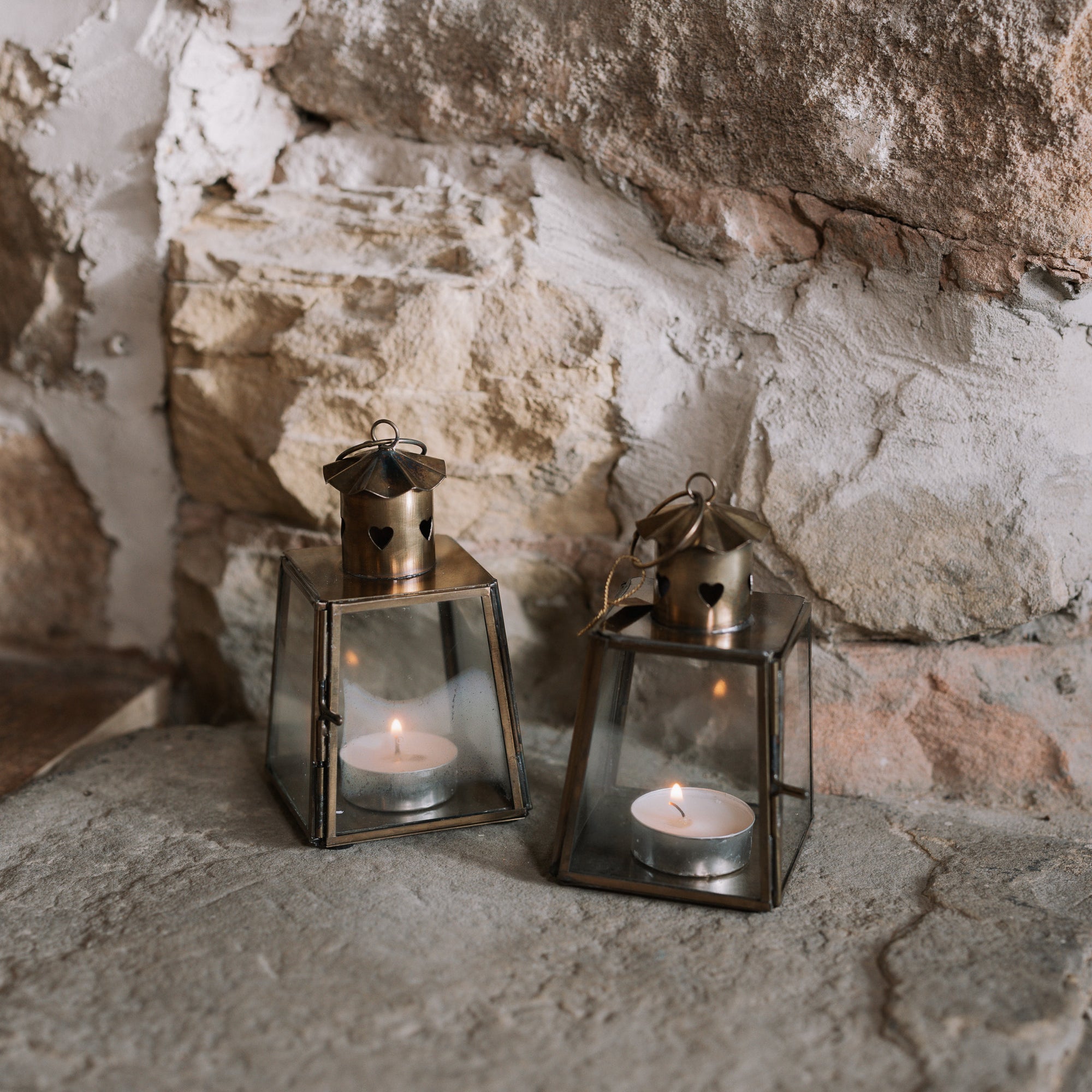 Two Mini bronze tealight candle lantern on stone hearth, with lit candles inside.