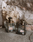 Two Mini bronze tealight candle lantern on stone hearth, with lit candles inside.