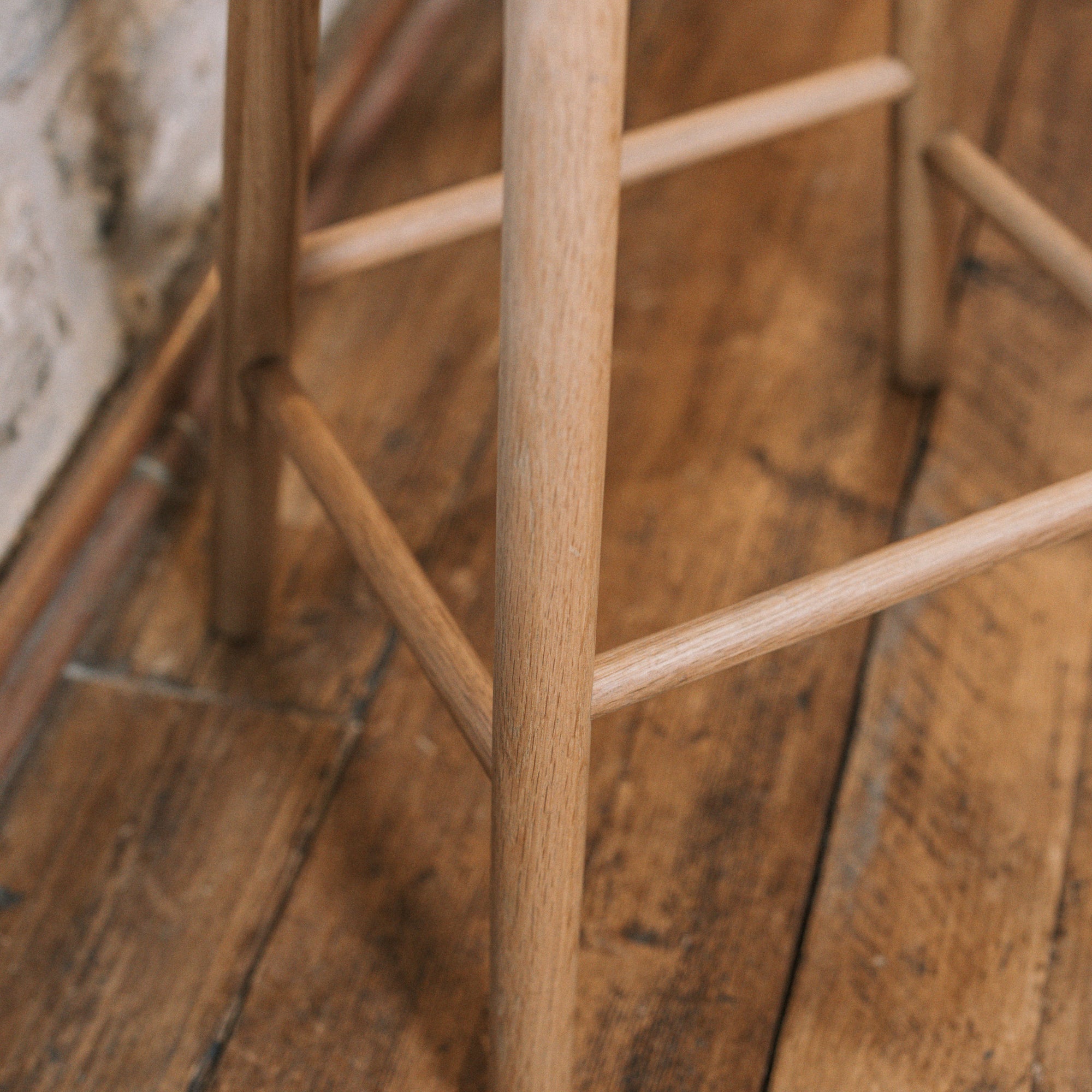 Natural wooden backless barstool against stone wall, shot of the leg.