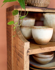 Close up of detailing on small wooden shelf with drawer, filled with crockery.