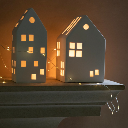 Two white porcelain house tealight holder filled with fairy lights in dark.