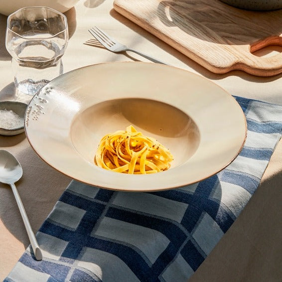 Off white speckled pasta plate with pasta inside on set table.